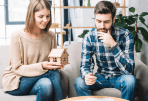 ouple discussing mortgage options while holding a model house indoors